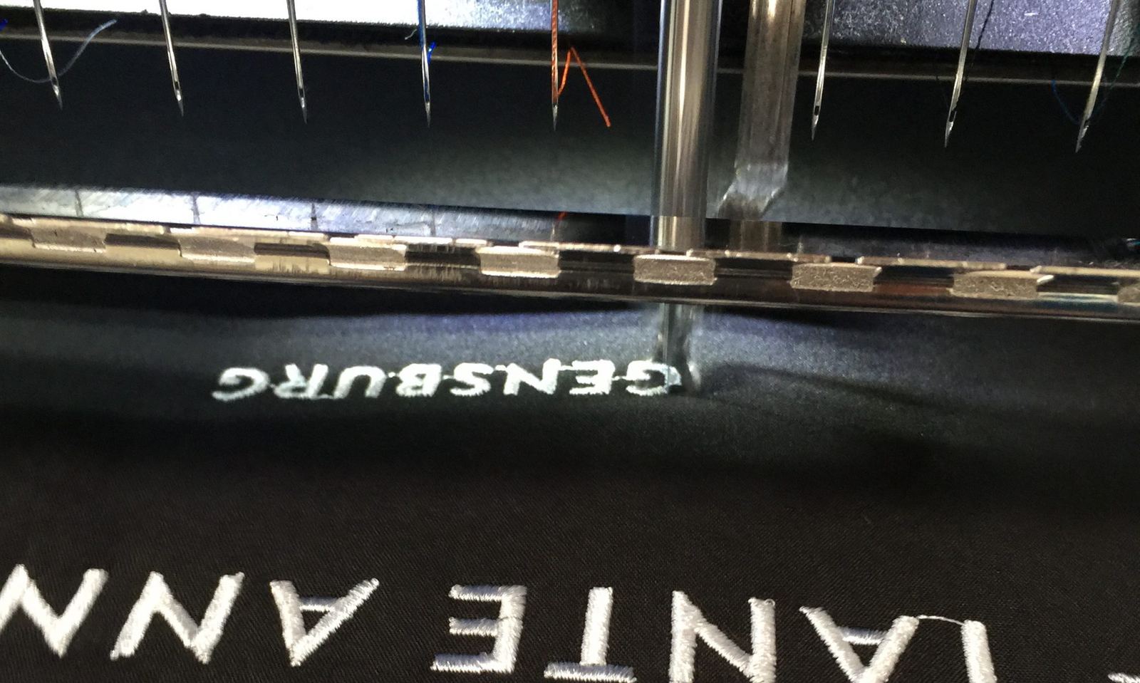 Stickmaschine stickt einen Schriftzug in ein dunkles Textil